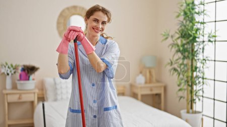 Téléchargez les photos : Jeune femme nettoyeur professionnel appuyé sur bâton serpillière souriant à la chambre - en image libre de droit