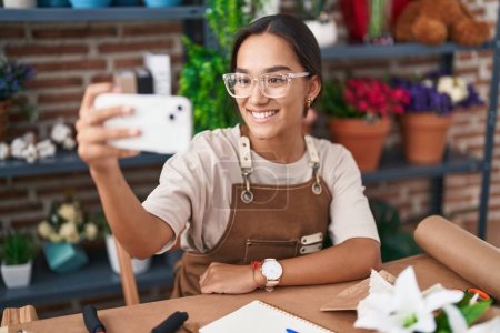 Photo for Young beautiful hispanic woman florist make selfie by smartphone sitting on table at florist - Royalty Free Image