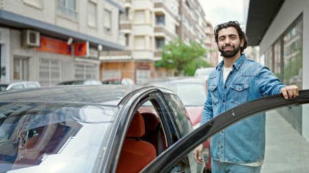 Téléchargez les photos : Jeune homme hispanique souriant confiant ouvrir la porte de la voiture à la rue - en image libre de droit