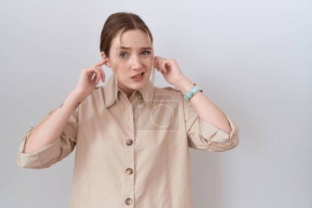 Foto de Mujer caucásica joven con camisa casual que cubre las orejas con los dedos con expresión molesta por el ruido de la música alta. concepto de sordo. - Imagen libre de derechos