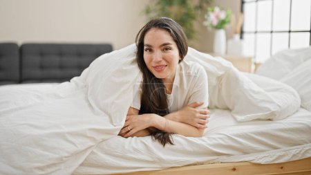 Photo for Young beautiful hispanic woman lying on bed covering with bedsheet at bedroom - Royalty Free Image