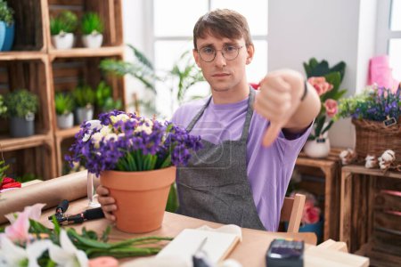 Téléchargez les photos : Homme blond caucasien travaillant à la boutique de fleuriste regardant malheureux et en colère montrant rejet et négatif avec les pouces vers le bas geste. mauvaise expression. - en image libre de droit