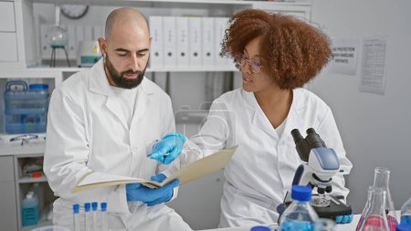 Foto de En el corazón de la ciencia, dos científicos resilientes, hablando y leyendo documentos de investigación médica innovadores juntos en el laboratorio. - Imagen libre de derechos