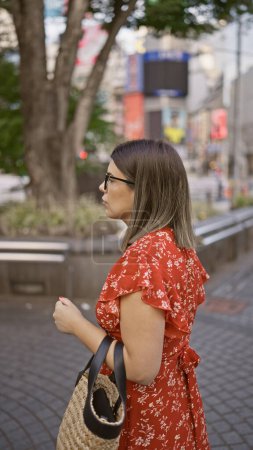 Photo for Beautiful hispanic woman in glasses gives an intense side look in tokyo's modern urban street while lost in concentration. - Royalty Free Image