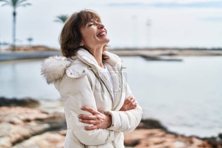 Téléchargez les photos : Femme d'âge moyen debout avec les bras croisés geste respirant au bord de la mer - en image libre de droit