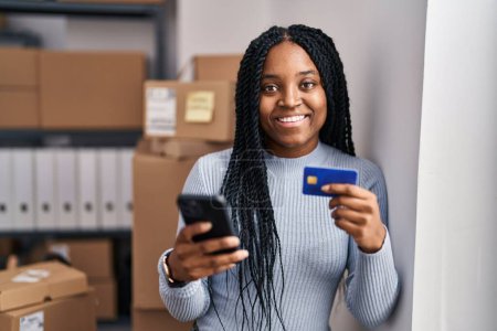 Foto de Trabajadora de negocios de comercio electrónico afroamericana usando teléfono inteligente y tarjeta de crédito en la oficina - Imagen libre de derechos