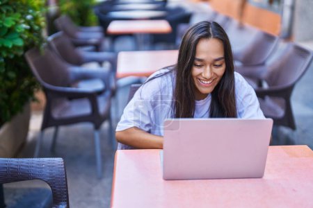 Photo for Young beautiful hispanic woman using laptop sitting on table at coffee shop terrace - Royalty Free Image