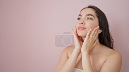 Foto de Mujer hispana hermosa joven masajeando la cara sobre un fondo rosa aislado - Imagen libre de derechos