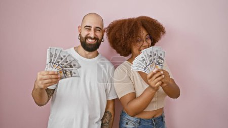 Photo for Confident beautiful couple smiling in love, standing together over an isolated pink background, casually holding dollars, enjoying a positive investment in their relationship and lifestyle. - Royalty Free Image