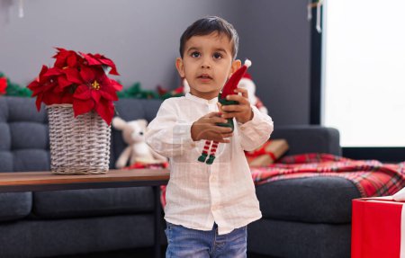 Foto de Adorable niño hispano sosteniendo juguete de pie por la decoración de Navidad en casa - Imagen libre de derechos