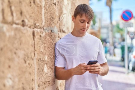 Téléchargez les photos : Jeune homme caucasien utilisant un smartphone avec une expression sérieuse à la rue - en image libre de droit