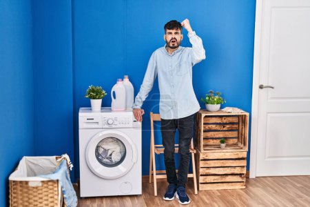 Photo for Young hispanic man with beard doing laundry standing at laundry room annoyed and frustrated shouting with anger, yelling crazy with anger and hand raised - Royalty Free Image