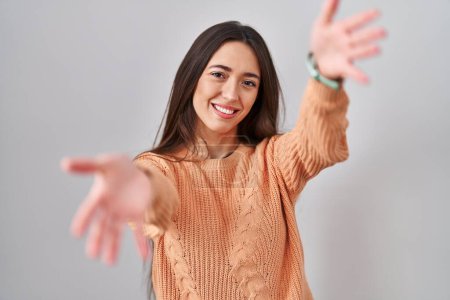 Téléchargez les photos : Jeune femme brune debout sur fond blanc regardant la caméra souriant à bras ouverts pour un câlin. expression joyeuse embrassant le bonheur. - en image libre de droit