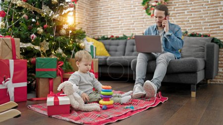 Foto de Padre e hijo celebrando la Navidad jugando con juguetes usando el portátil en casa - Imagen libre de derechos