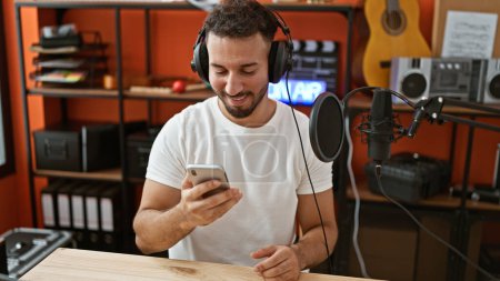 Foto de Joven músico árabe con auriculares usando smartphone en estudio de música - Imagen libre de derechos