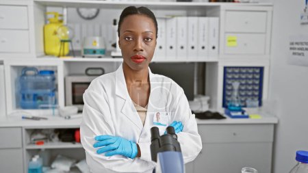 Foto de Científica afroamericana seria, con los brazos cruzados, se sienta en el laboratorio médico, comprendiendo profundamente la belleza de la ciencia - Imagen libre de derechos