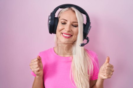 Photo for Caucasian woman listening to music using headphones excited for success with arms raised and eyes closed celebrating victory smiling. winner concept. - Royalty Free Image