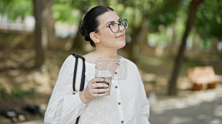 Photo for Young beautiful hispanic woman smiling drinking take away coffee at the park - Royalty Free Image