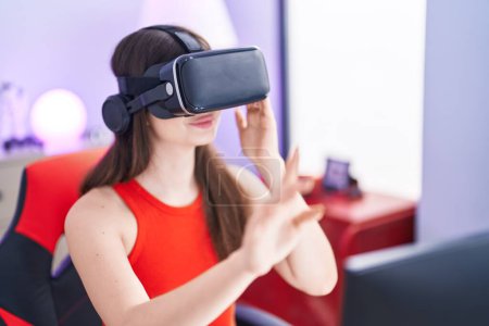 Téléchargez les photos : Jeune femme caucasienne streamer jouer à un jeu vidéo en utilisant des lunettes de réalité virtuelle à la salle de jeu - en image libre de droit
