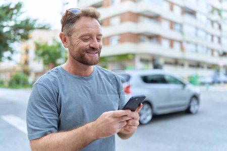 Foto de Hombre de mediana edad sonriendo confiado usando teléfono inteligente en la calle - Imagen libre de derechos