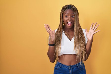 Photo for African american woman with braided hair standing over yellow background celebrating crazy and amazed for success with arms raised and open eyes screaming excited. winner concept - Royalty Free Image