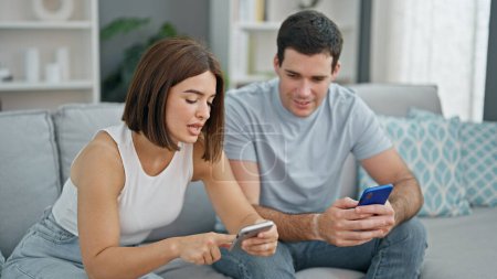 Photo for Beautiful couple sitting on sofa together using smartphones at home - Royalty Free Image