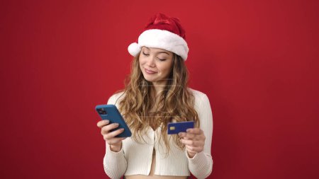 Photo for Young beautiful hispanic woman wearing christmas hat using smartphone and credit card over isolated red background - Royalty Free Image