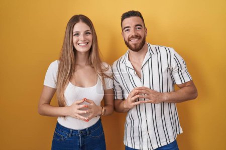 Téléchargez les photos : Jeune couple debout sur fond jaune mains ensemble et doigts croisés souriant détendu et joyeux. succès et optimisme - en image libre de droit