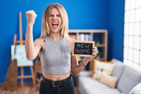 Photo for Blonde caucasian woman holding blackboard with new home text annoyed and frustrated shouting with anger, yelling crazy with anger and hand raised - Royalty Free Image