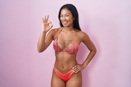 Téléchargez les photos : Femme hispanique portant un bikini souriant positif faire ok signe avec la main et les doigts. expression réussie. - en image libre de droit