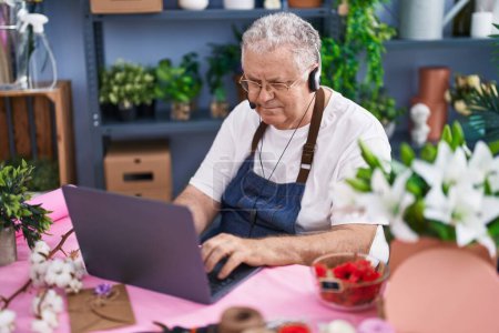 Photo for Middle age grey-haired man florist using laptop and headphones at florist - Royalty Free Image