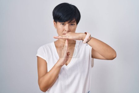 Photo for Young asian woman with short hair standing over isolated background doing time out gesture with hands, frustrated and serious face - Royalty Free Image