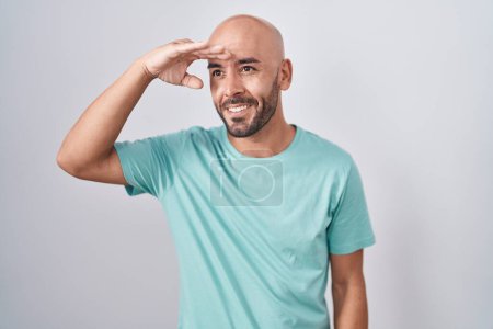 Photo for Middle age bald man standing over white background very happy and smiling looking far away with hand over head. searching concept. - Royalty Free Image