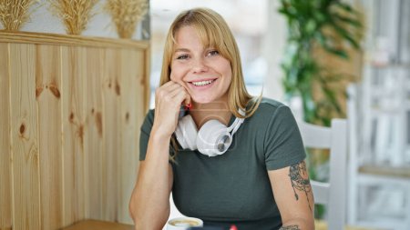 Téléchargez les photos : Jeune femme blonde souriante confiante assise sur la table au café - en image libre de droit