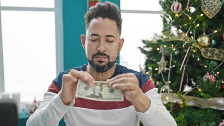Foto de Joven latino rompiendo billetes de 20 dólares celebrando la Navidad en casa - Imagen libre de derechos
