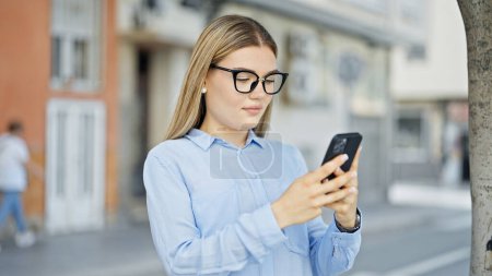 Téléchargez les photos : Jeune femme blonde travailleuse d'affaires utilisant un smartphone avec une expression sérieuse dans la rue - en image libre de droit