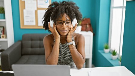 Foto de Trabajadora de negocios afroamericana usando laptop con auriculares en la oficina - Imagen libre de derechos