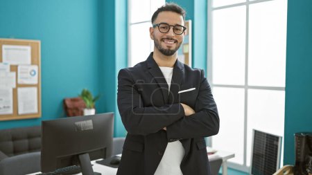 Téléchargez les photos : Jeune homme arabe homme d'affaires debout avec les bras croisés geste souriant au bureau - en image libre de droit