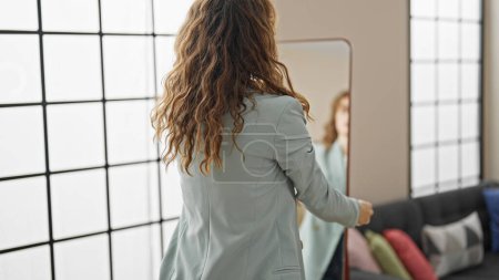 Téléchargez les photos : Jeune femme regardant sur miroir portant une veste à la maison - en image libre de droit
