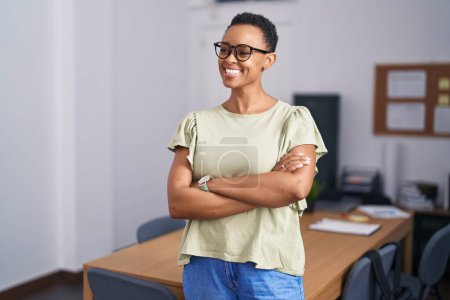 Téléchargez les photos : Afro-américaine femme d'affaires souriant confiance debout avec les bras croisés geste au bureau - en image libre de droit