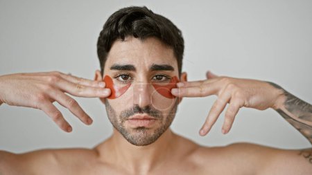 Photo for Young hispanic man standing shirtless putting baggy eyes patches over isolated white background - Royalty Free Image