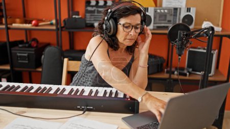 Foto de Mujer hispana de mediana edad tocando el piano teniendo una lección en línea en el estudio de música - Imagen libre de derechos