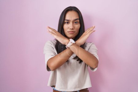 Photo for Young hispanic woman standing over pink background rejection expression crossing arms doing negative sign, angry face - Royalty Free Image
