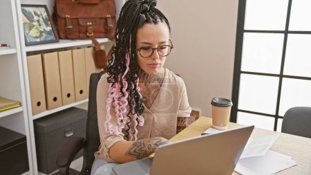 Foto de Mujer hispana joven y hermosa enfocada trabajando duro en su computadora portátil en la oficina, encarnando el éxito y el profesionalismo - Imagen libre de derechos