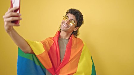 Téléchargez les photos : Jeune homme hispanique portant drapeau arc-en-ciel ayant appel vidéo sur fond jaune isolé - en image libre de droit