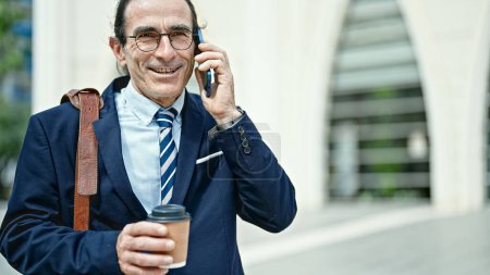 Téléchargez les photos : Moyen âge homme d'affaires travailleur tenant café parler sur smartphone à la rue - en image libre de droit