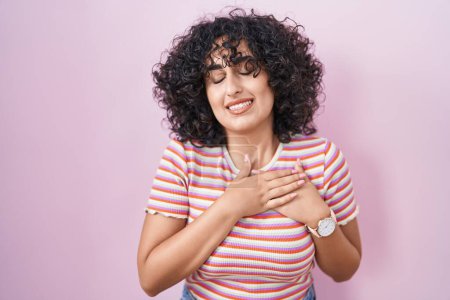 Téléchargez les photos : Jeune femme du Moyen-Orient debout sur fond rose souriant avec les mains sur la poitrine avec les yeux fermés et geste reconnaissant sur le visage. concept de santé. - en image libre de droit