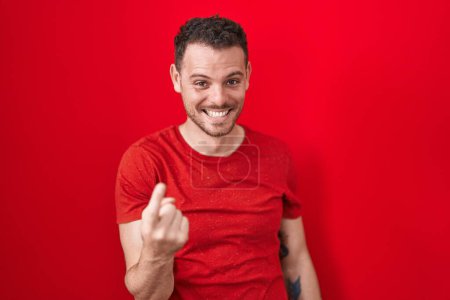 Téléchargez les photos : Jeune homme hispanique debout sur fond rouge signe venir ici geste avec la main invitant accueillant heureux et souriant - en image libre de droit