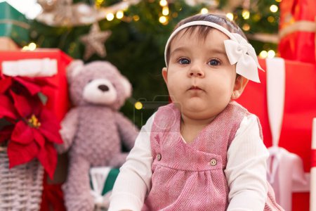 Photo for Adorable hispanic baby sitting on floor by christmas tree at home - Royalty Free Image