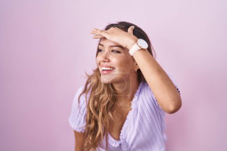 Photo for Young hispanic woman standing over pink background very happy and smiling looking far away with hand over head. searching concept. - Royalty Free Image